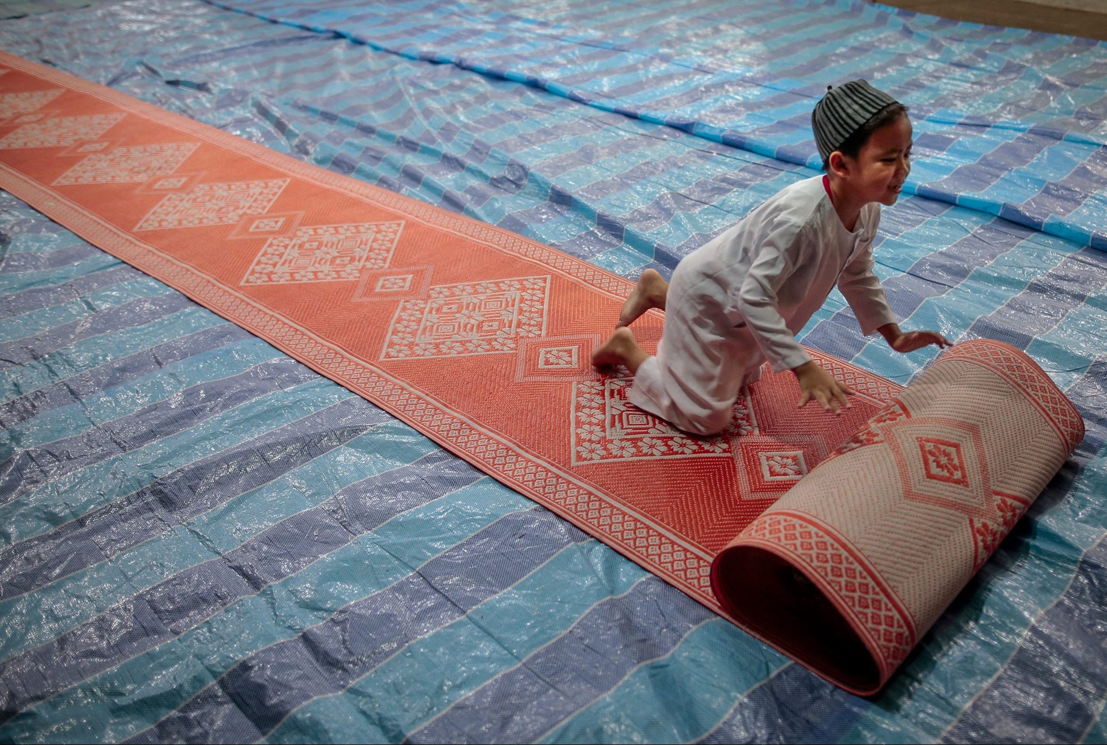 Een jongen rolt een gebedsmat uit in Singapore, speciaal voor het tarawieh gebed. Tijdens dit avondgebed wordt de vastendag afgesloten.