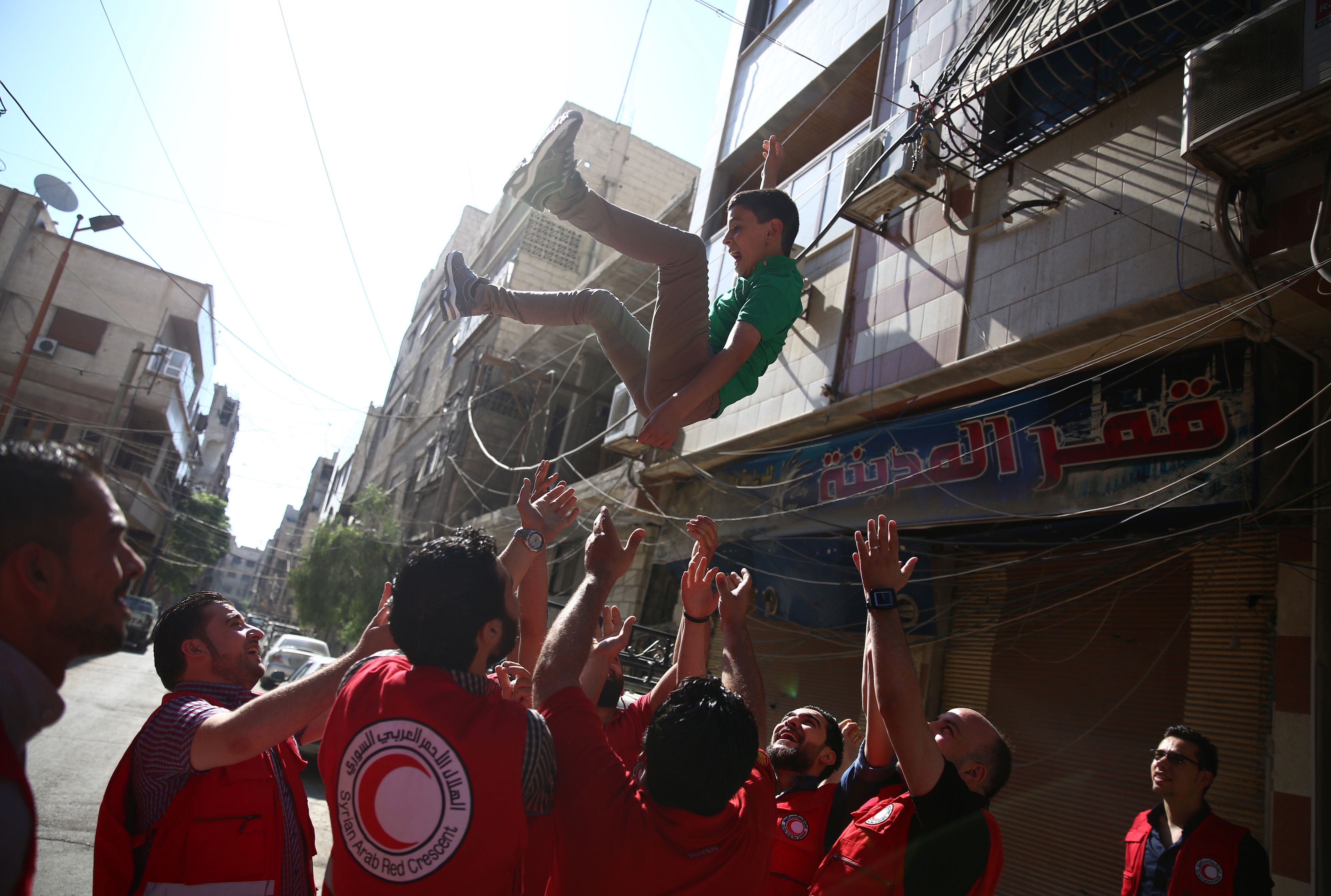 2016-07-06 08:34:49 Members of the Syrian Arab Red Crescent (SARC) throw a young boy under a psychological support program in the air in the rebel-held town of Douma, east of the capital Damascus, as they celebrate the first day of Eid al-Fitr, which marks the end of the Muslim fasting month of Ramadan on July 6, 2016. / AFP PHOTO / Abd Doumany