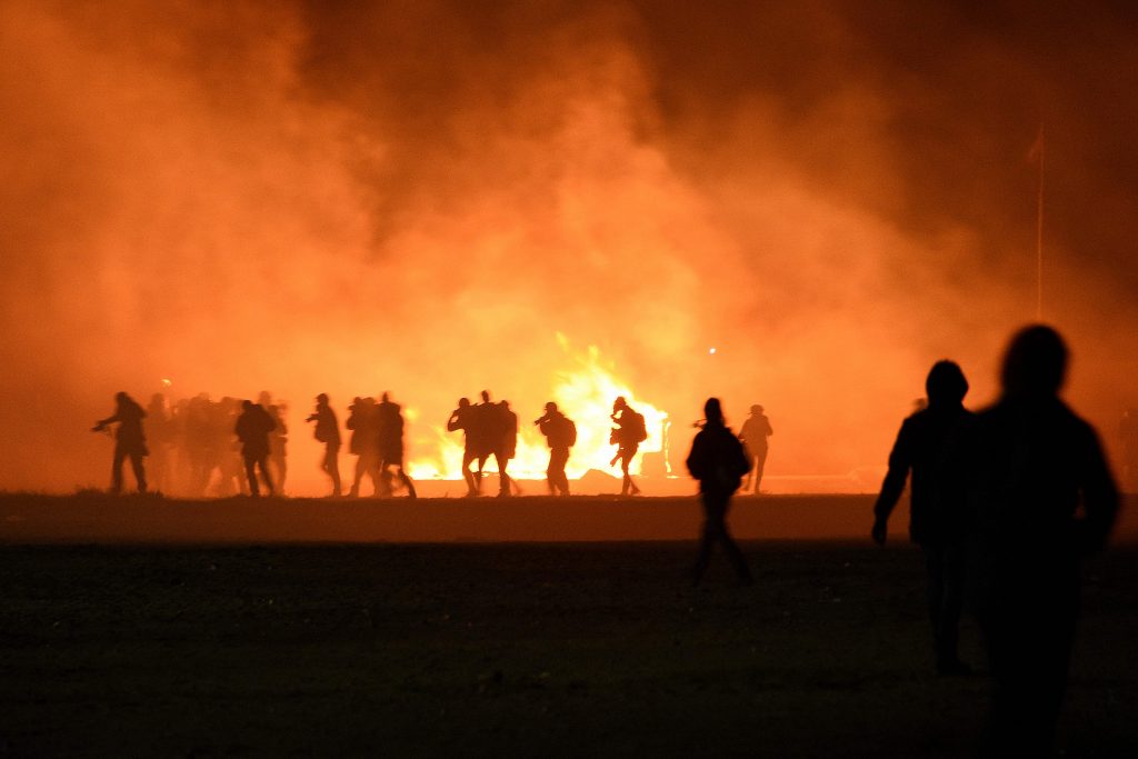 2016-10-23 20:27:08 TOPSHOT - Smoke billows as migrants start a fire during clashes with police at the "Jungle" migrant camp in Calais, northern France, on October 23, 2016 on the eve of the camp's planned evacuation. On the eve of the demolition of the Calais "Jungle" camp, French officials handed out flyers in several languages notifying migrants of the camp's imminent closure and urging them to abandon their dreams of reaching Britain. / AFP PHOTO / DENIS CHARLET